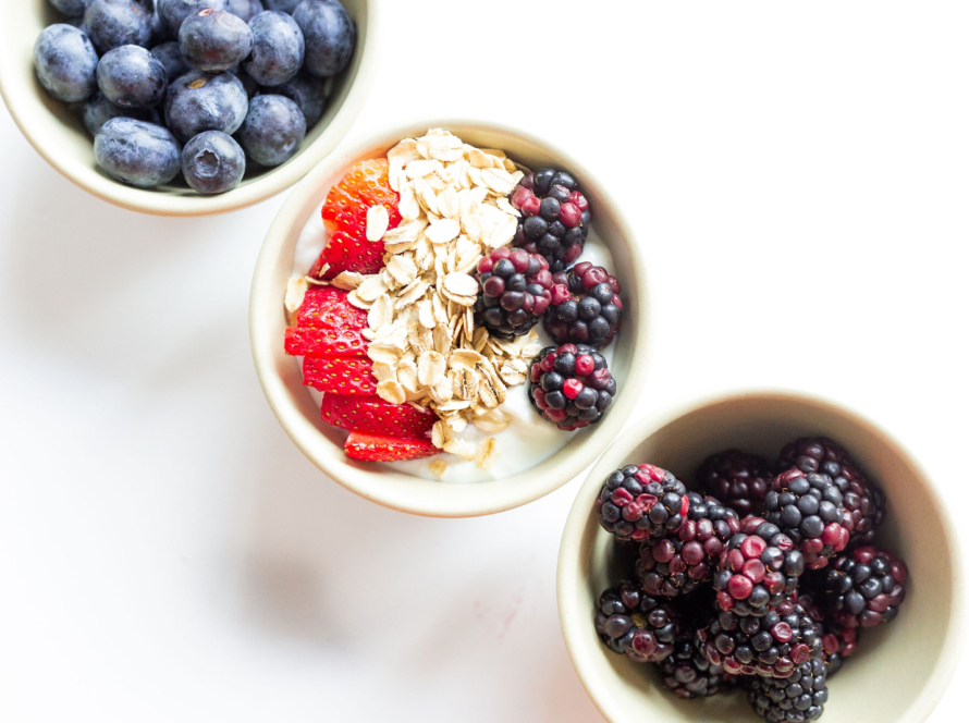3 off white bowls on a white backdrop positioned diagonally. One has blackberries, one has blueberries, and the middle one has raspberrys, granola, straberries on top of oatmeal.