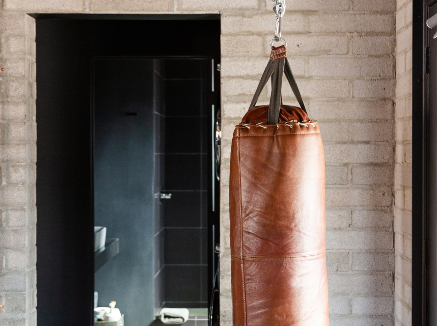 We see a large brown punching bag hanging from the ceiling and in the background a partial view of a bathroom.