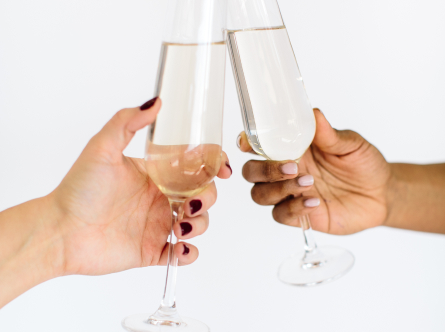 The image shows two women's hands (one black and one white) toasting with champagne glasses.