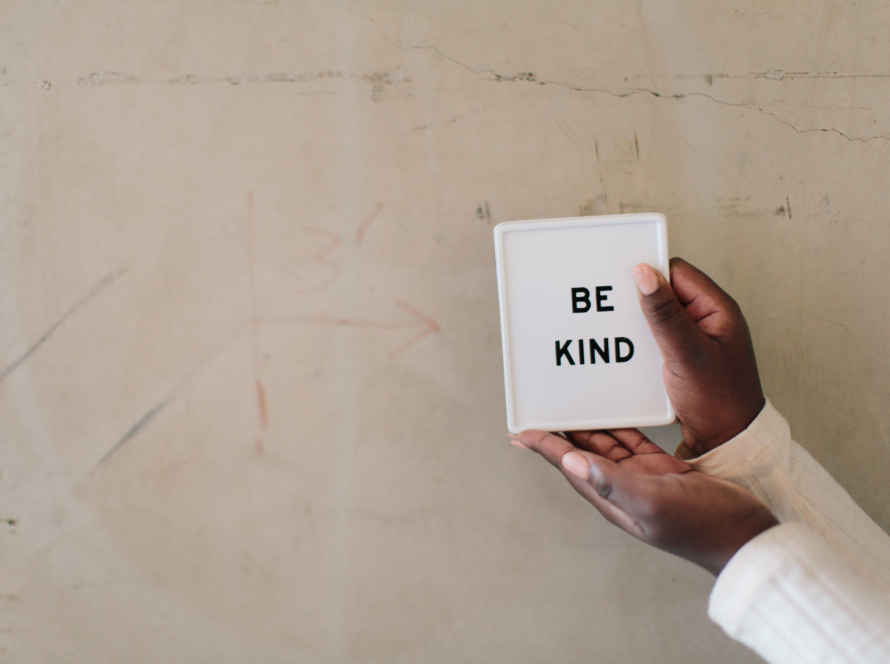 In the image we can see the hands of a black man holding a small box with a white background and a black lettering with the legend "be kind".