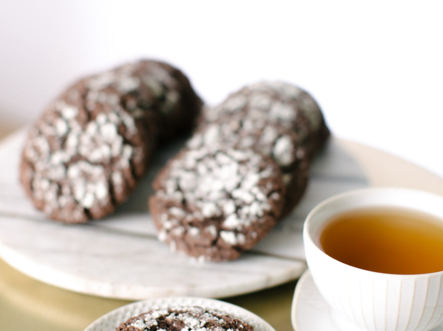 In the image we can see a cup of tea, and also a plate of chocolate cookies.