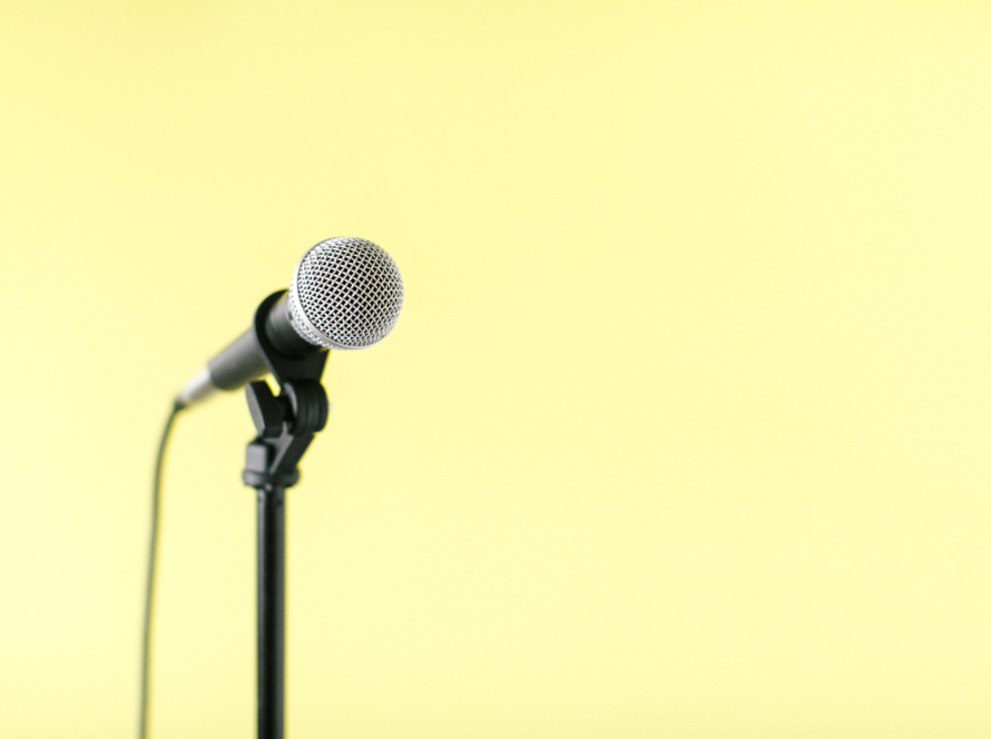 In the image we can see a microphone on its stand and a yellow background.