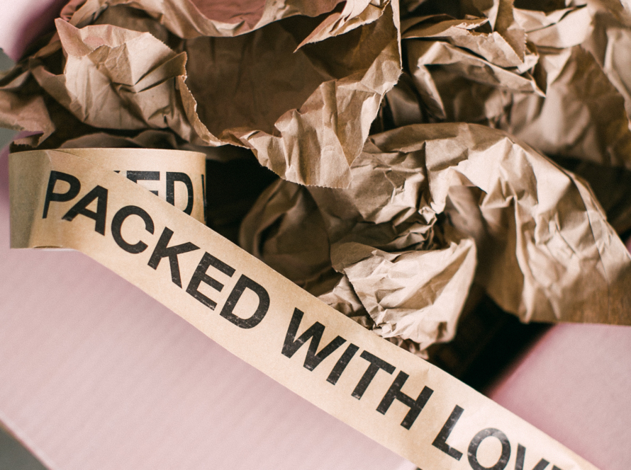 In the image we can see a box, with wrapping paper inside and a ribbon with the legend "packaged with love"