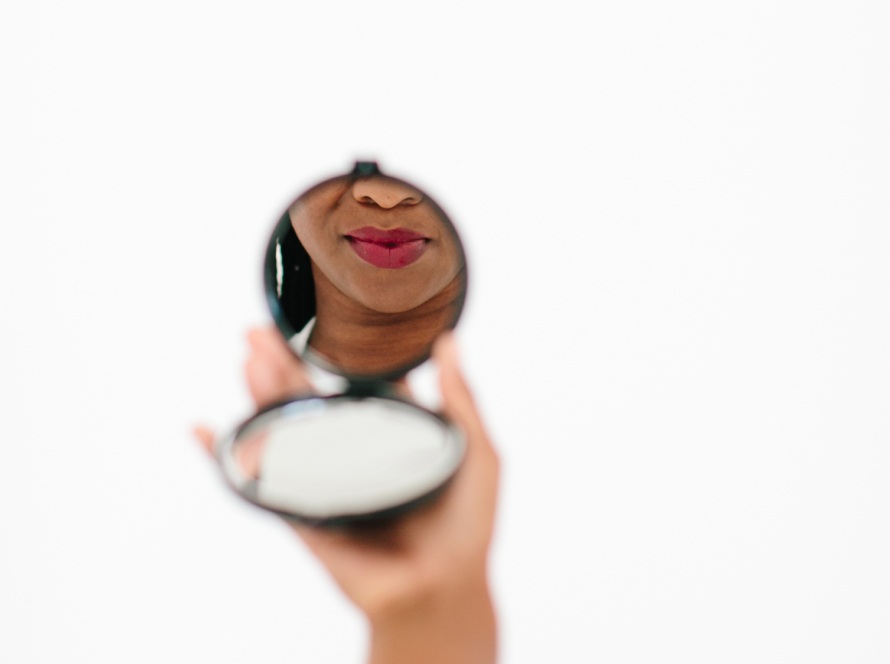 In the image we can see the lower face of a black woman reflecting in a hand mirror.
