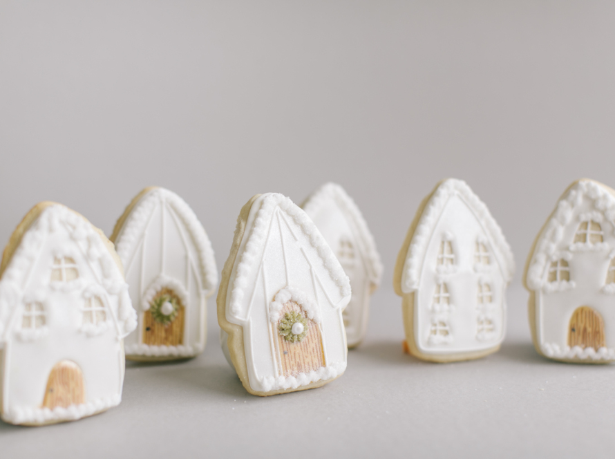 In the image we can see some cookies decorated with very delicate house shapes in white and pastel tones.