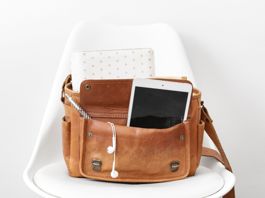 In the image we can see in a brown women's purse, a tablet and headphones, both white, and further back, an agenda/notebook.