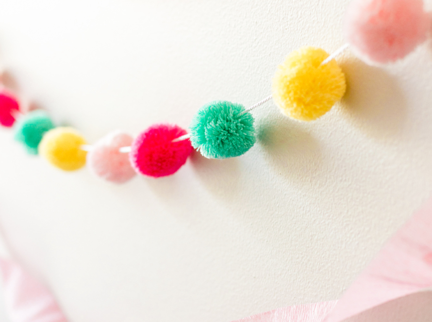 In the image, we can see a necklace made with thread and several cotton pompoms of different colors.