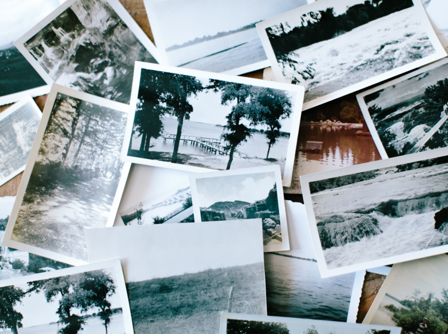 In the image, we can see a number of vintage-style photos, on photographic paper, with white, grey and black tones, which portray landscapes with vegetation and bodies of water such as lakes, rivers and waterfalls.