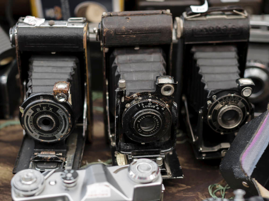 In the image, we can see a modern digital camera surrounded by several old cameras.