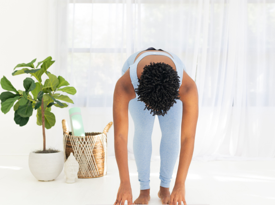 In the image, we can see a black woman, doing physical exercises on a blue mat, in a white room decorated with a green plant.